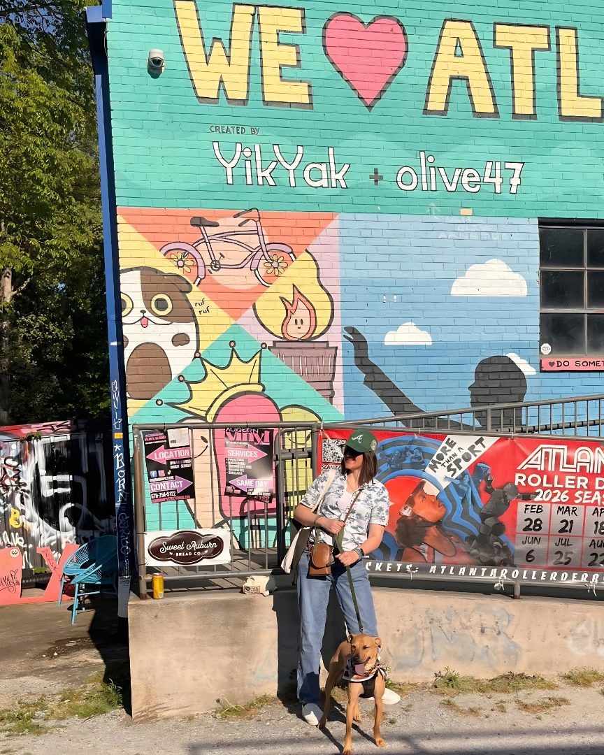 Eve with a tan pup on a leash in front of the colorful We Love ATL mural